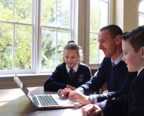 Technology image. Male teacher with two students, all looking at the computer together.